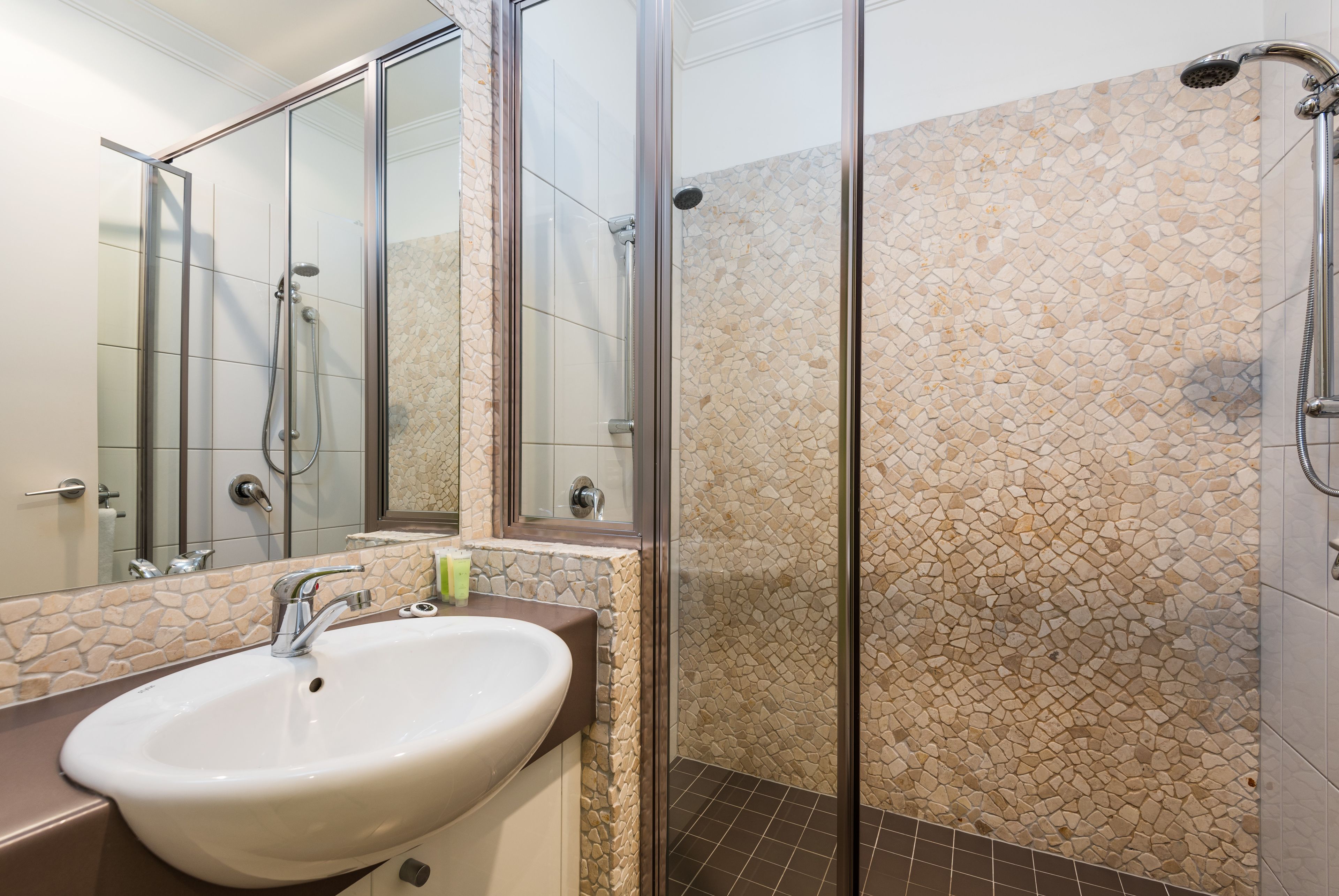 A bathroom with a glass-enclosed shower, a white sink, and a stone mosaic wall.