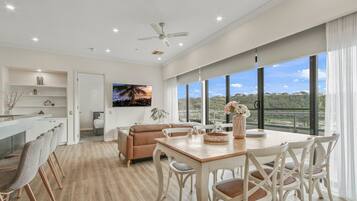 A spacious living area with a dining table, chairs, a sofa, and a TV mounted on the wall.