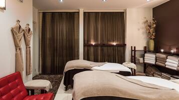 Relax in a serene spa room with two massage tables, a comfortable sofa, and a peaceful atmosphere.
