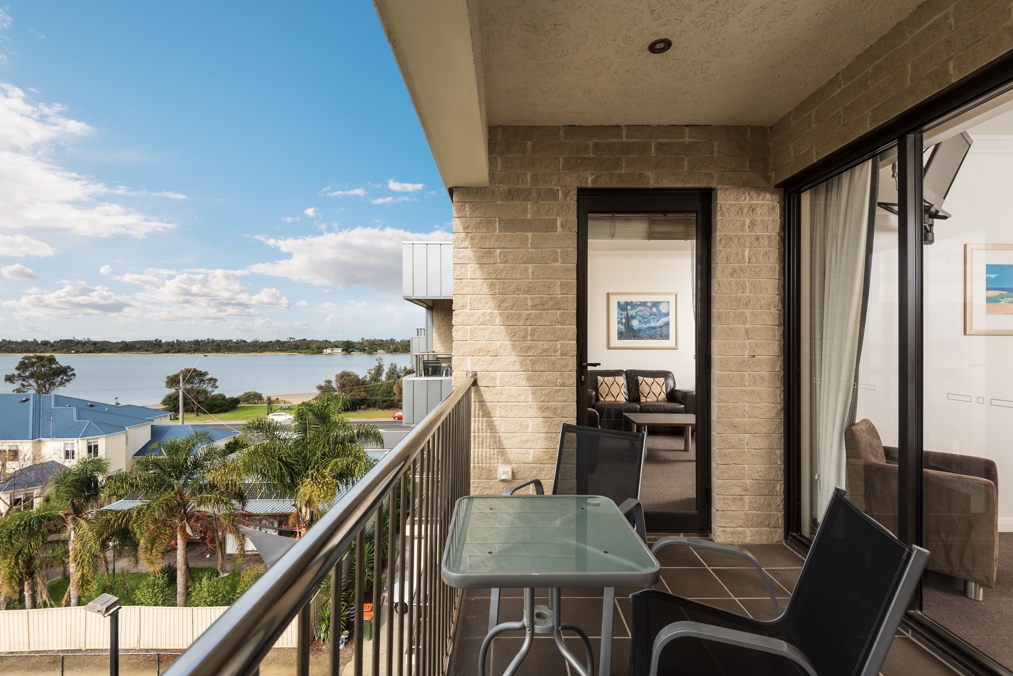 A balcony with a glass table and chairs, a view of the sea, and a brick wall.