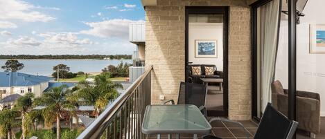 A balcony with a glass table and chairs, a view of the sea, and a brick wall.