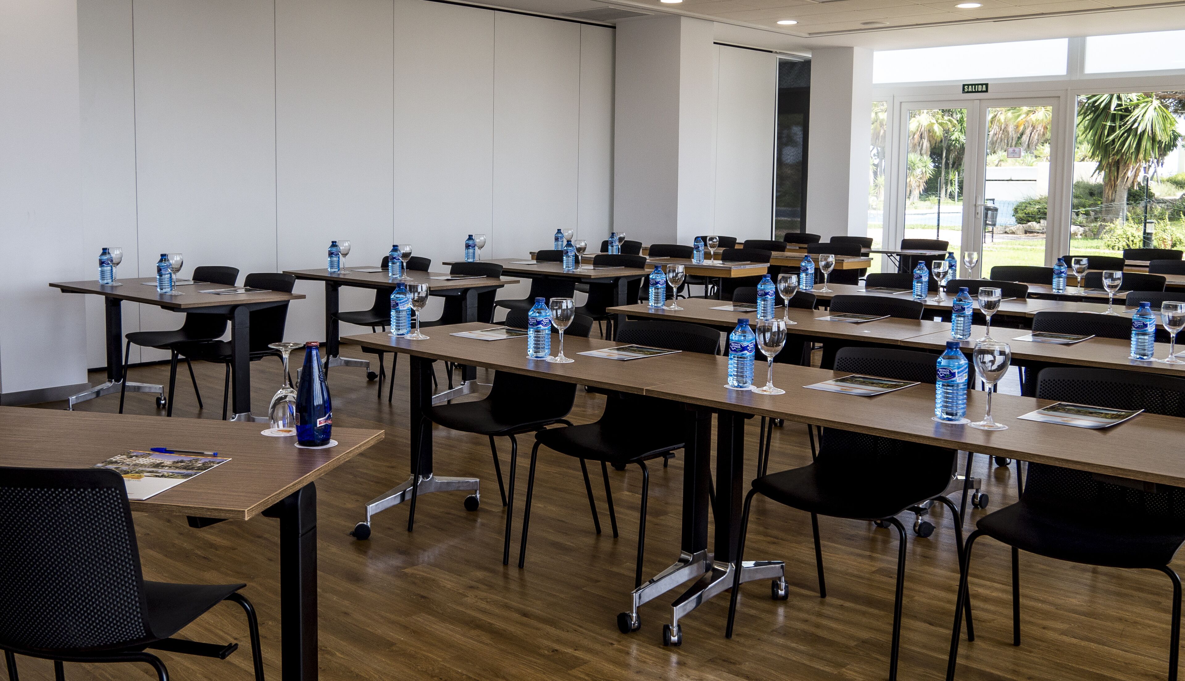 Un salón de conferencias con mesas, sillas, botellas de agua y copas de vino.