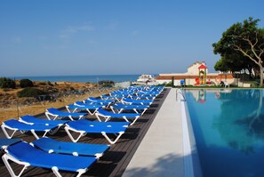Zona de piscina con sillas reclinables azules y una vista despejada del mar.
