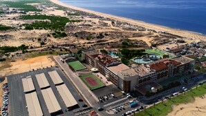 An aerial view of a coastal hotel with a large parking area, a tennis court, and a pool. - Gran Hotel del Coto (Almonte)