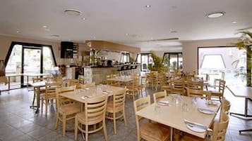Un restaurante amplio con varias mesas y sillas, ventanas grandes y una cocina visible al fondo.