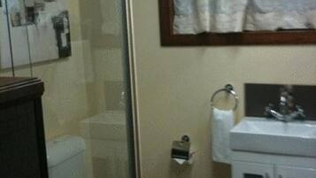 Un baño con cabina de ducha de vidrio, inodoro, lavabo con espejo y perchero.