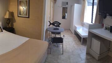 Habitación de hotel compacta con cama, una pequeña mesa con silla, microondas y televisión.