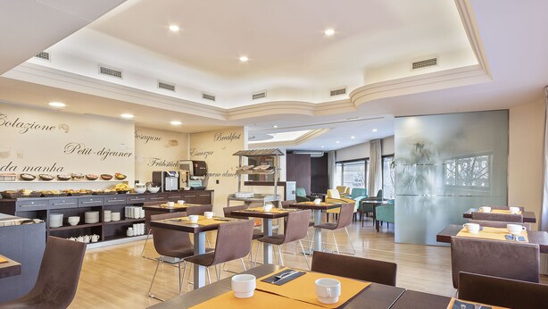 A modern cafe with multiple seating areas, a coffee machine, and a wall with breakfast-related text.