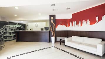 Eine Hotelhalle mit einer Rezeption, einem weißen Sofa, einer Uhr und einem Stadtbild-Wandgemälde.