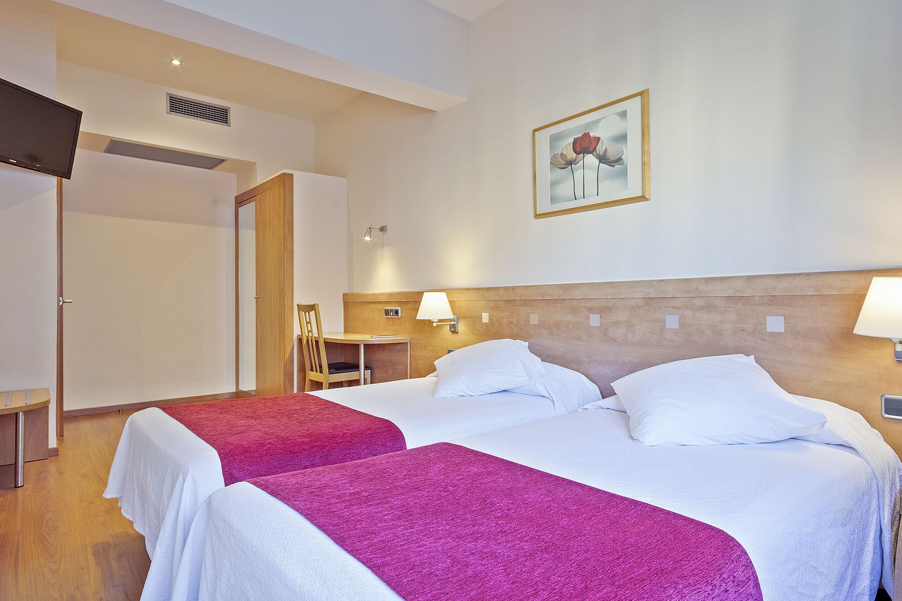 A hotel room with two beds, a desk, a chair, and a painting on the wall.