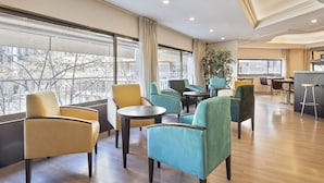 A modern hotel lobby with seating areas, large windows, and a view of the city.