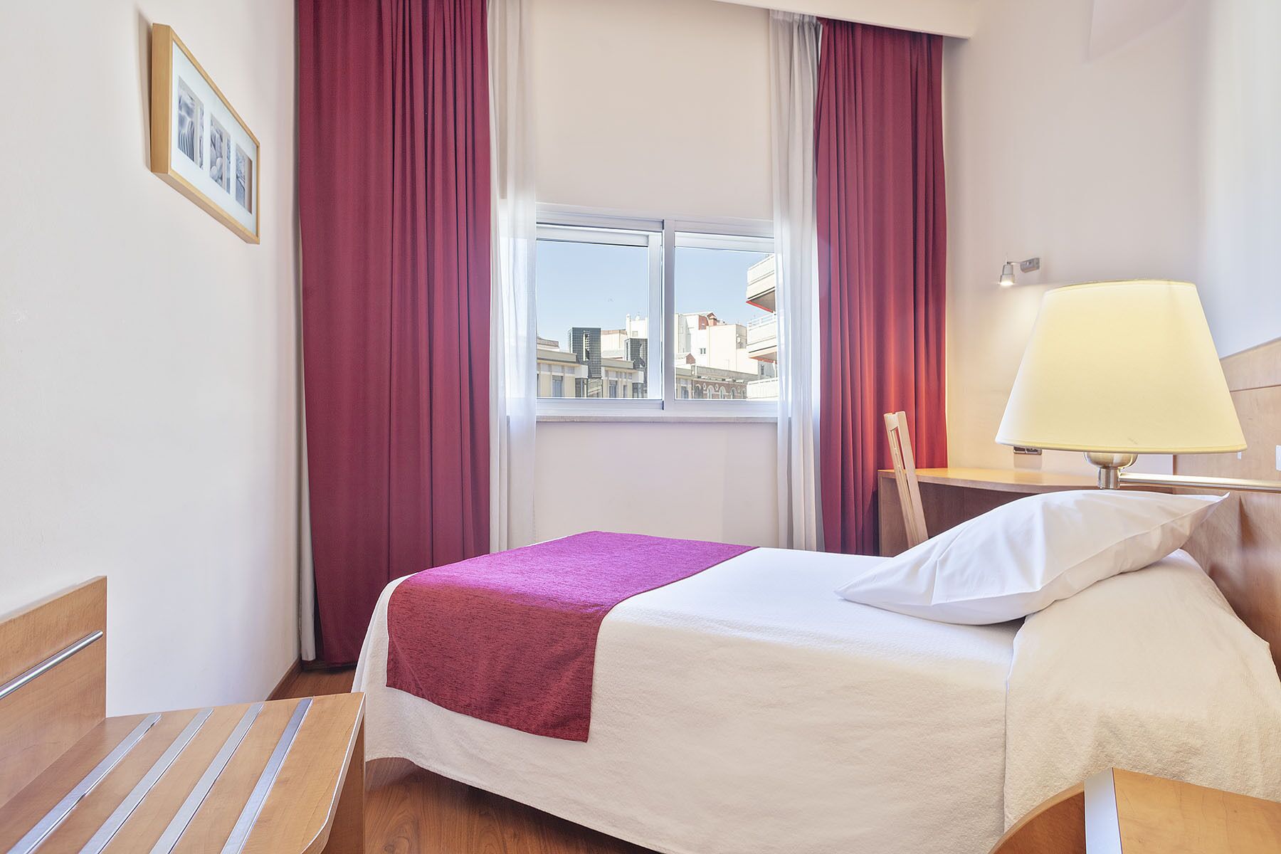 Ein Hotelzimmer mit Bett, Fenster, Lampe und Blick auf die Stadt.