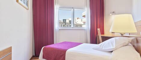 Ein Hotelzimmer mit Bett, Fenster, Lampe und Blick auf die Stadt.