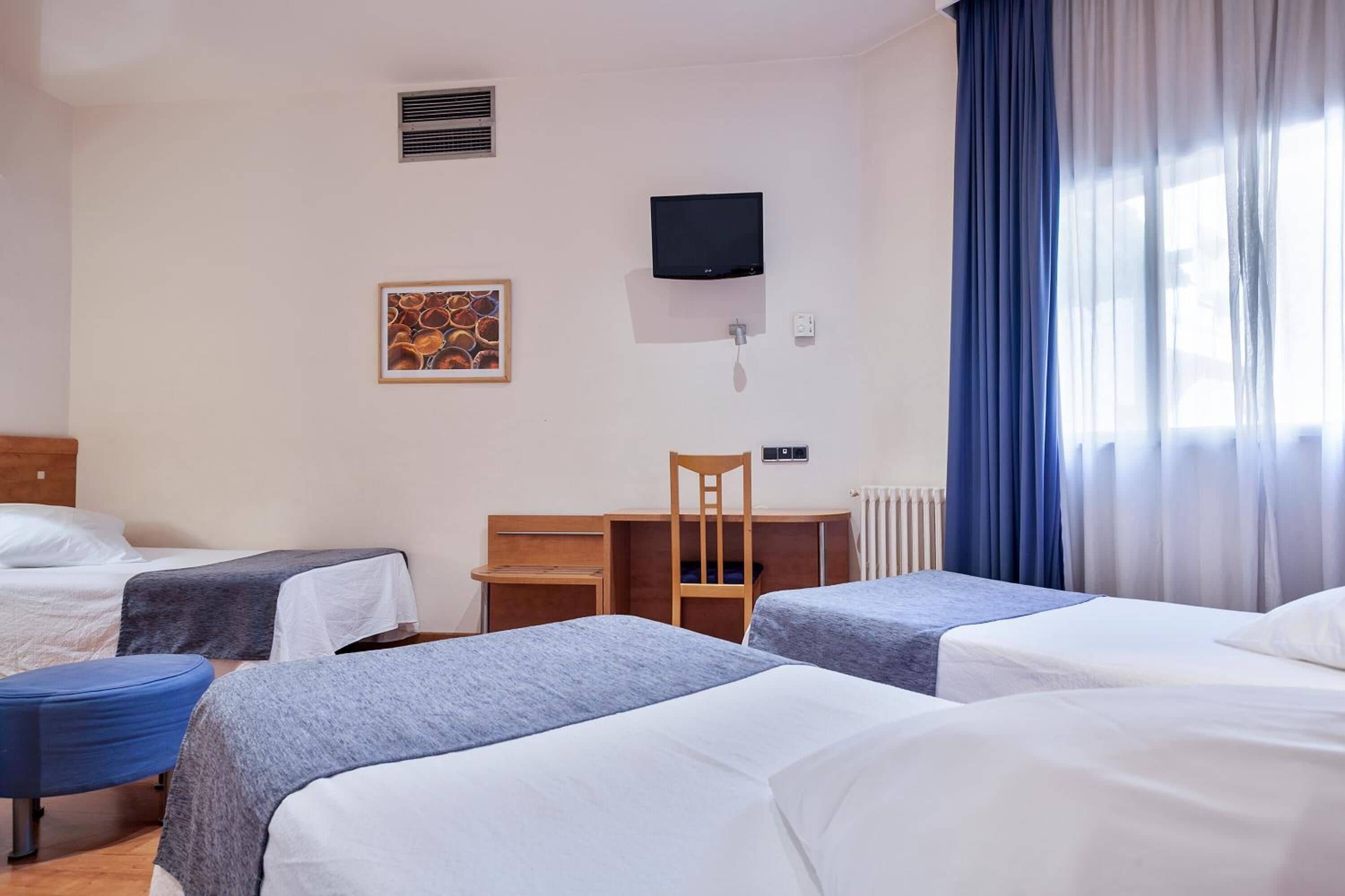 A hotel room with two single beds, a desk, a chair, a TV, and a radiator.