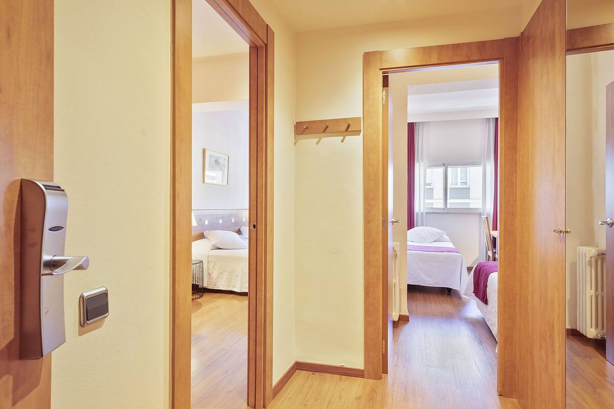 A hallway leading to two bedrooms with wooden flooring, a coat rack, and a wall-mounted light fixture.