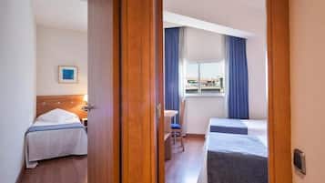Een hotelkamer met twee bedden, een bureau en een raam met gordijnen.