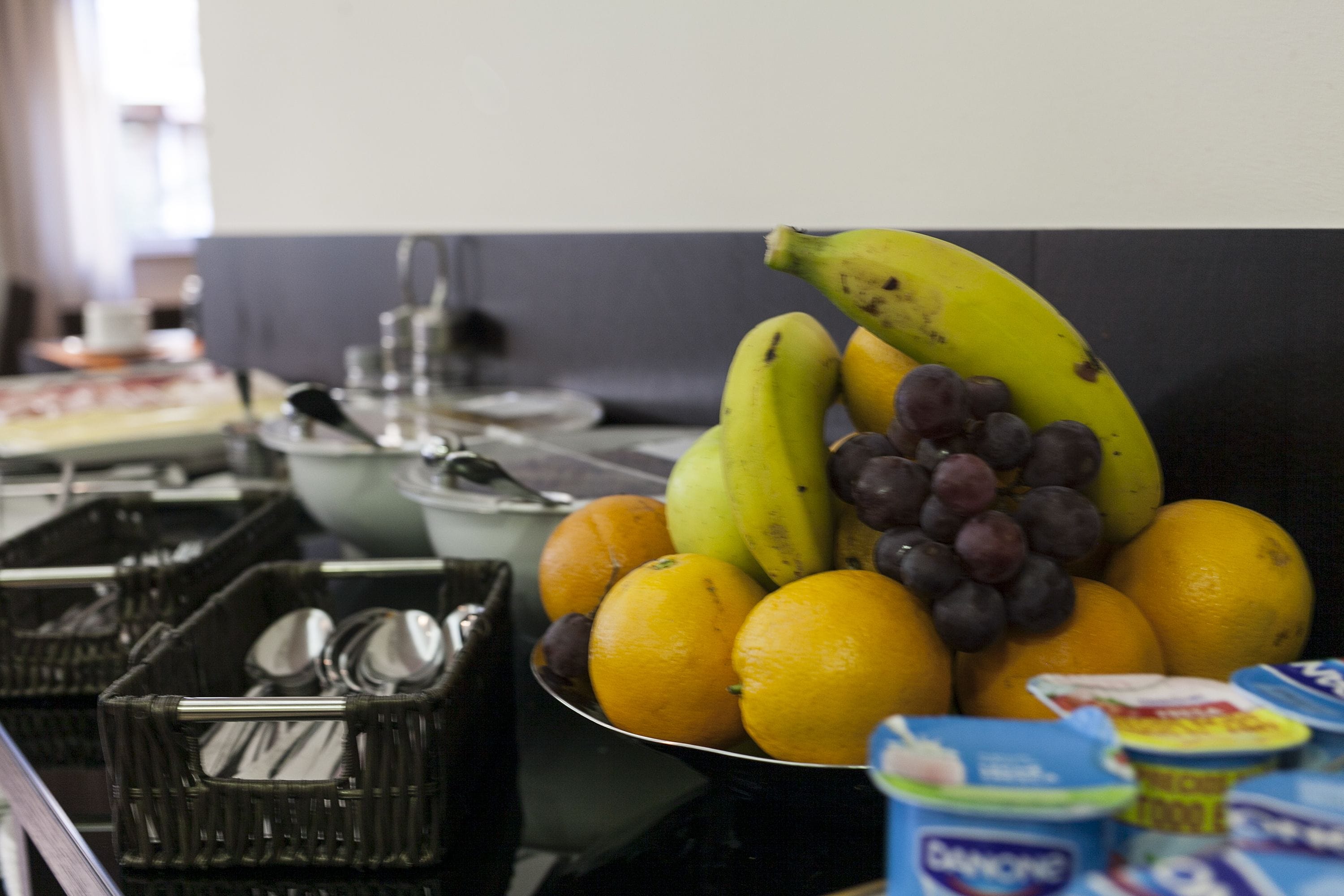 Una mesa de buffet con frutas, como plátanos, uvas y naranjas, y diferentes recipientes de comida.
