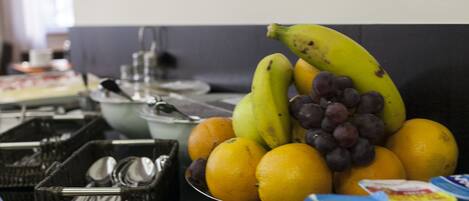 Una mesa de buffet con frutas, como plátanos, uvas y naranjas, y diferentes recipientes de comida.