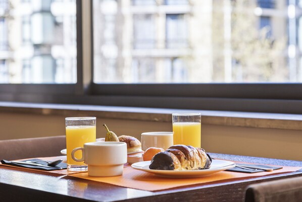 A breakfast setting with croissants, juice, and coffee on a table by a window.