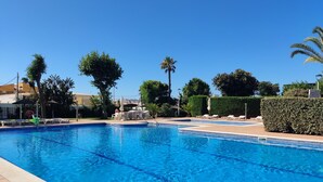 A clear blue swimming pool with lounge chairs and umbrellas, surrounded by greenery and a hedge. - Pato Amarillo (Punta Umbría)