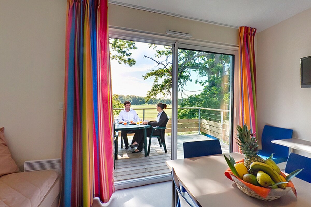 A room with a sliding glass door leading to an outdoor area, a dining table with chairs, and a fruit bowl on the table.