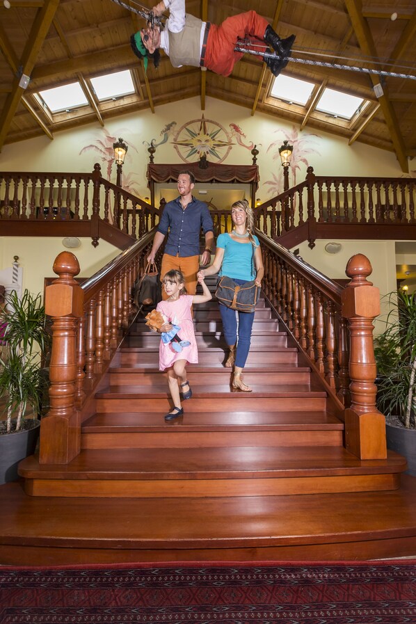 A family ascending a wooden staircase with a high ceiling and skylights.