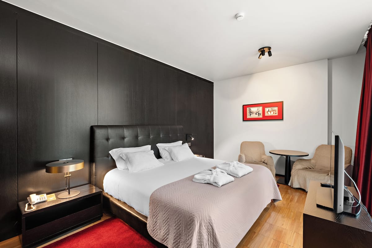 Une chambre d’hôtel comprenant un lit, une table de chevet avec une lampe, une chaise, un téléviseur et une petite table.