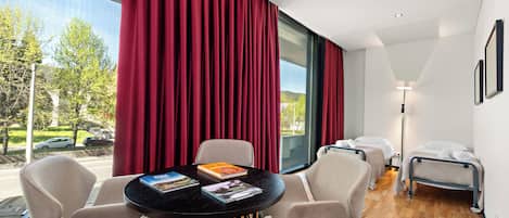 Una habitación de hotel con un ventanal grande, una mesa redonda con sillas, dos camas y una lámpara.