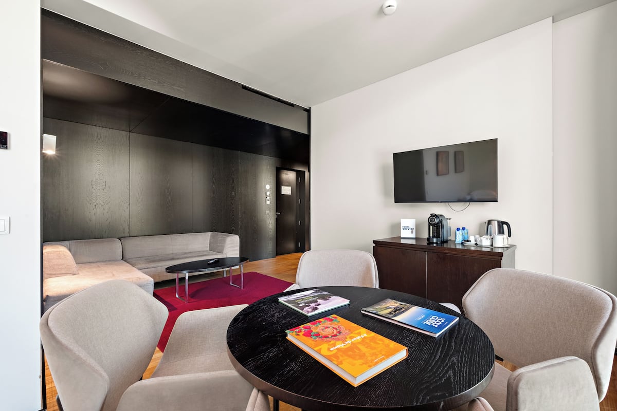 Een moderne woonruimte met een bank, stoelen, een ronde tafel met boeken, een flatscreen televisie en een koffiehoek.