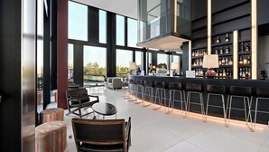 Un espace bar moderne doté de hauts plafonds, de grandes fenêtres et de différents types de sièges, notamment des tabourets et des chaises de bar.
