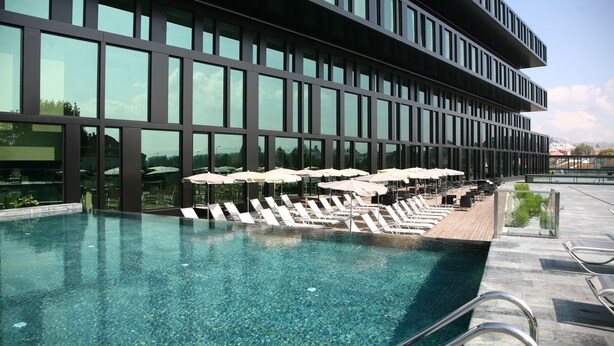 Un hôtel moderne doté d’une grande piscine extérieure, de chaises longues et de parasols.