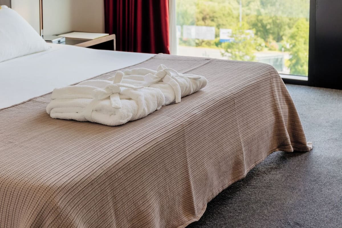 Een hotelkamer met een bed, een rood gordijn, uitzicht op een stadsgezicht en een groot raam.