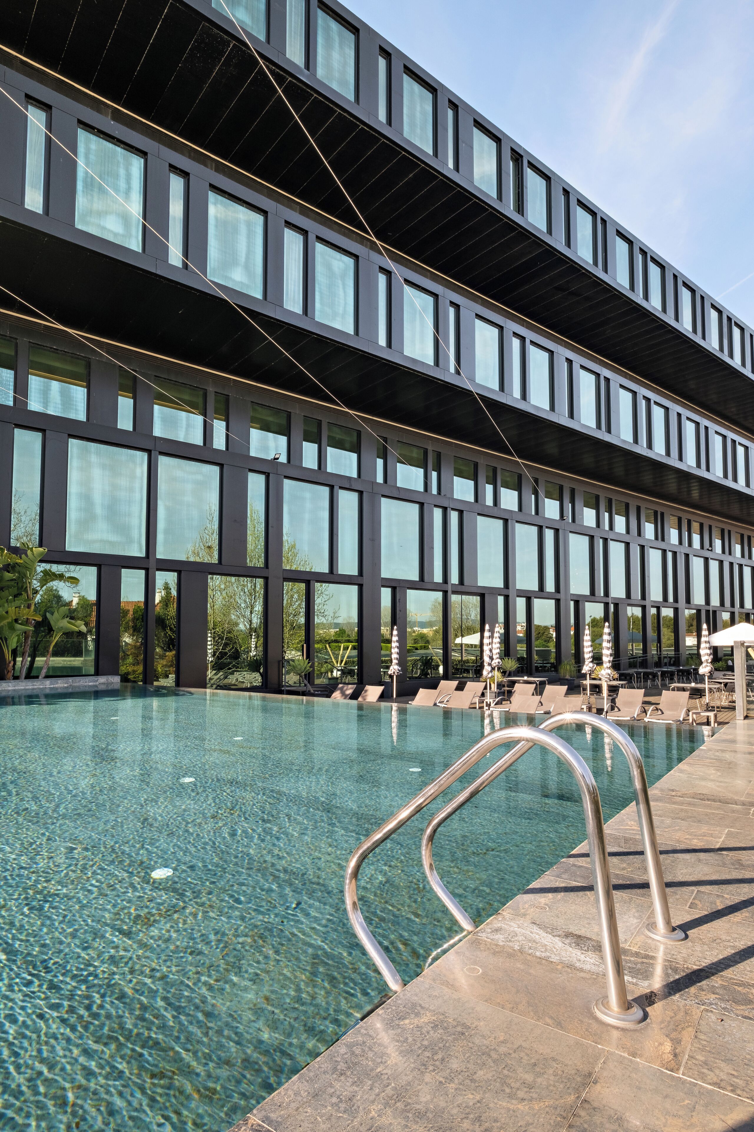 Un edifici modern amb una gran piscina, aigua cristal·lina i baranes metàl·liques.