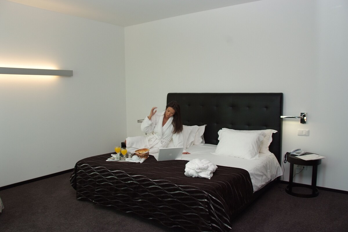 Ein Hotelzimmer mit Bett, Laptop, Bademantel und Nachttisch mit Telefon.