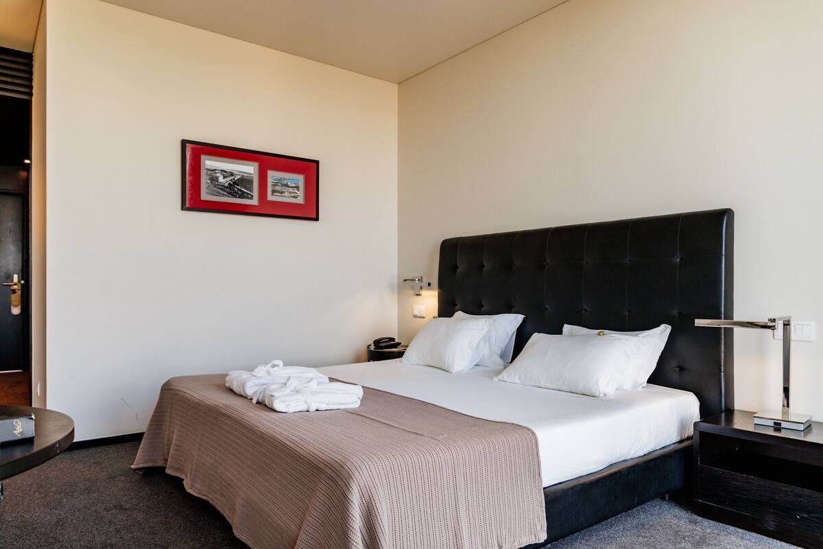 Een hotelkamer met een groot bed, een nachtkastje, een nachttafel, een ingelijst beeld aan de muur en een deur.