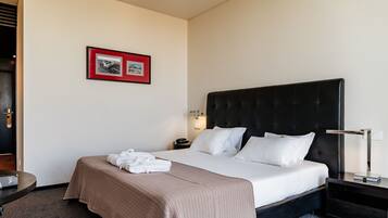 A hotel room with a large bed, a bedside table, a nightstand, a framed picture on the wall, and a door.