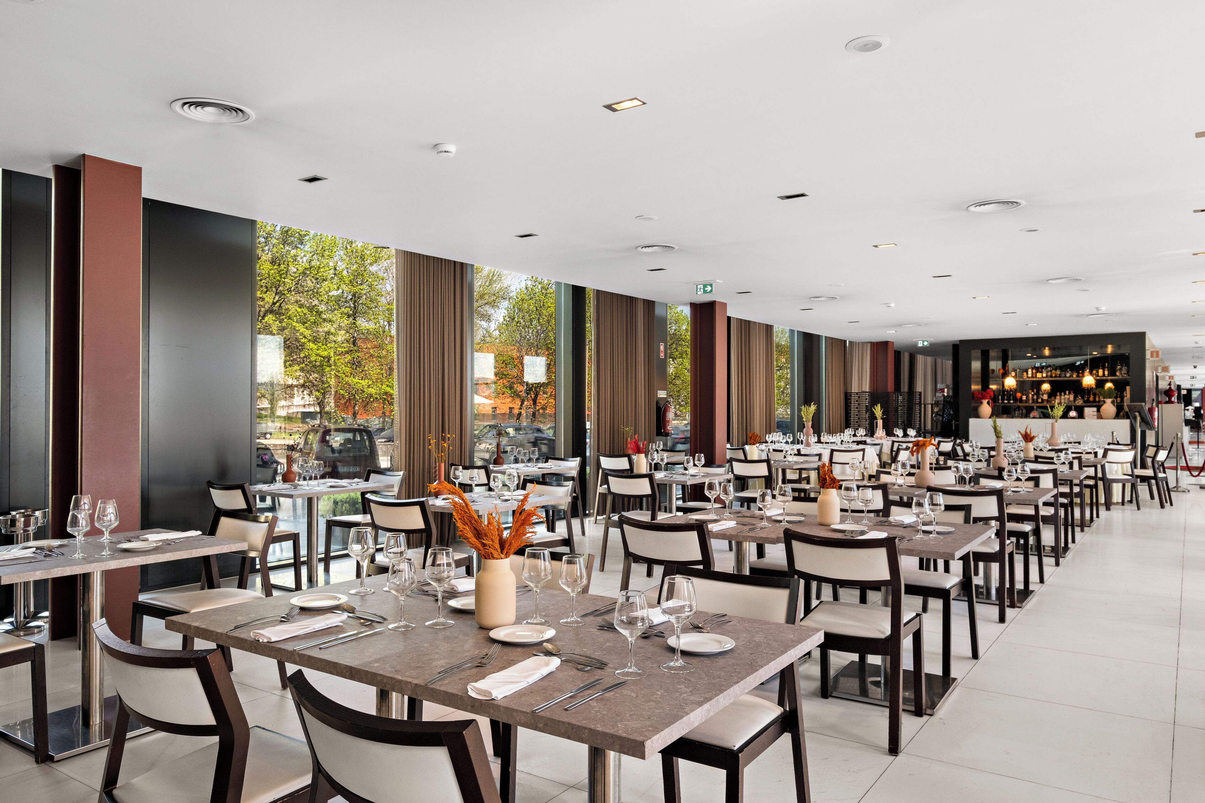 A restaurant with tables set for dining, a bar area, and large windows offering a view of the outside.