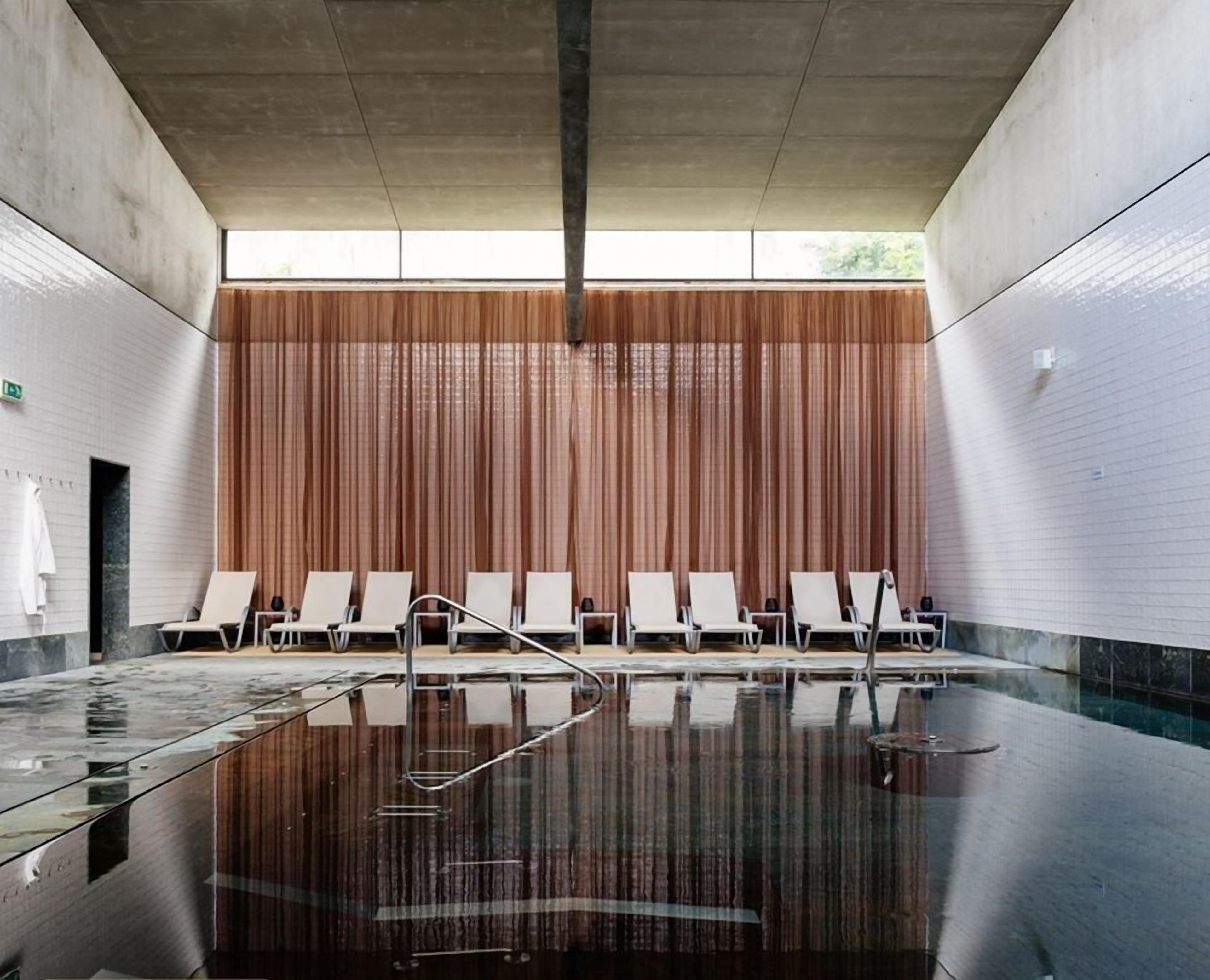A modern indoor swimming pool with a glass floor, wooden panel walls, and white lounge chairs.