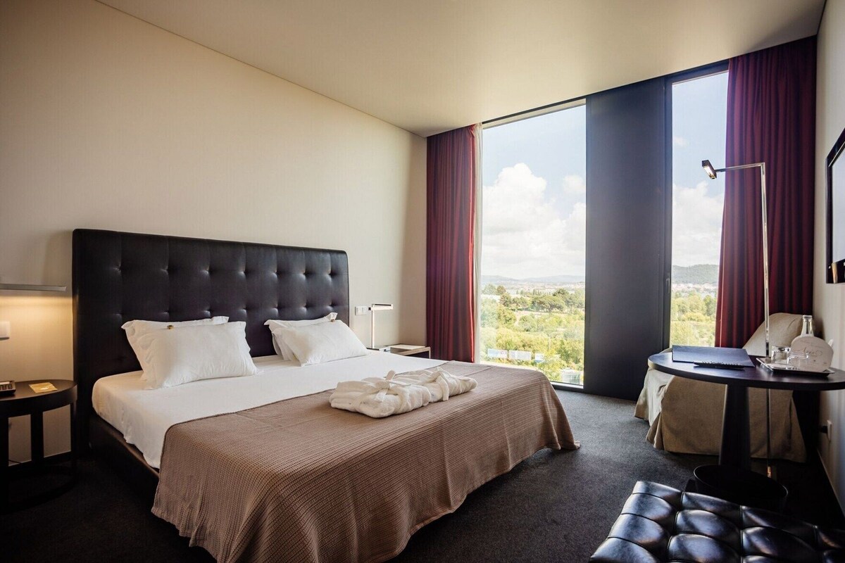 A hotel room with a large bed, a desk, and a view of the outdoors.
