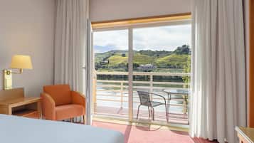 Habitación de hotel con cama, escritorio, silla, mesa y balcón con vistas al campo.