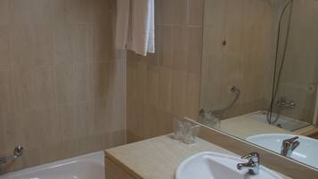 Un baño con bañera, lavamanos, espejo y toallero.