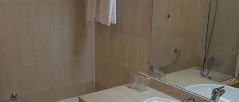 Un baño con bañera, lavamanos, espejo y toallero.
