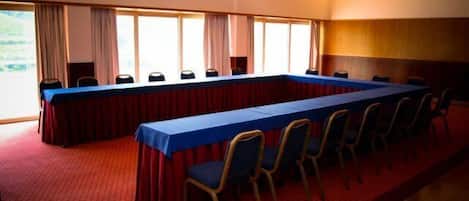 Un salón de conferencias con una larga mesa, sillas y ventanas amplias.
