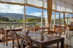 Un restaurante con terraza al aire libre con vistas a un viñedo y colinas.