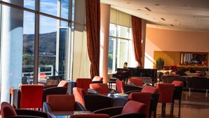 A spacious dining area with red chairs and a piano, large windows with curtains, and a view of the hills.