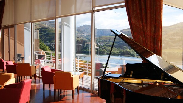 A grand piano in a spacious room with large windows overlooking a scenic landscape.