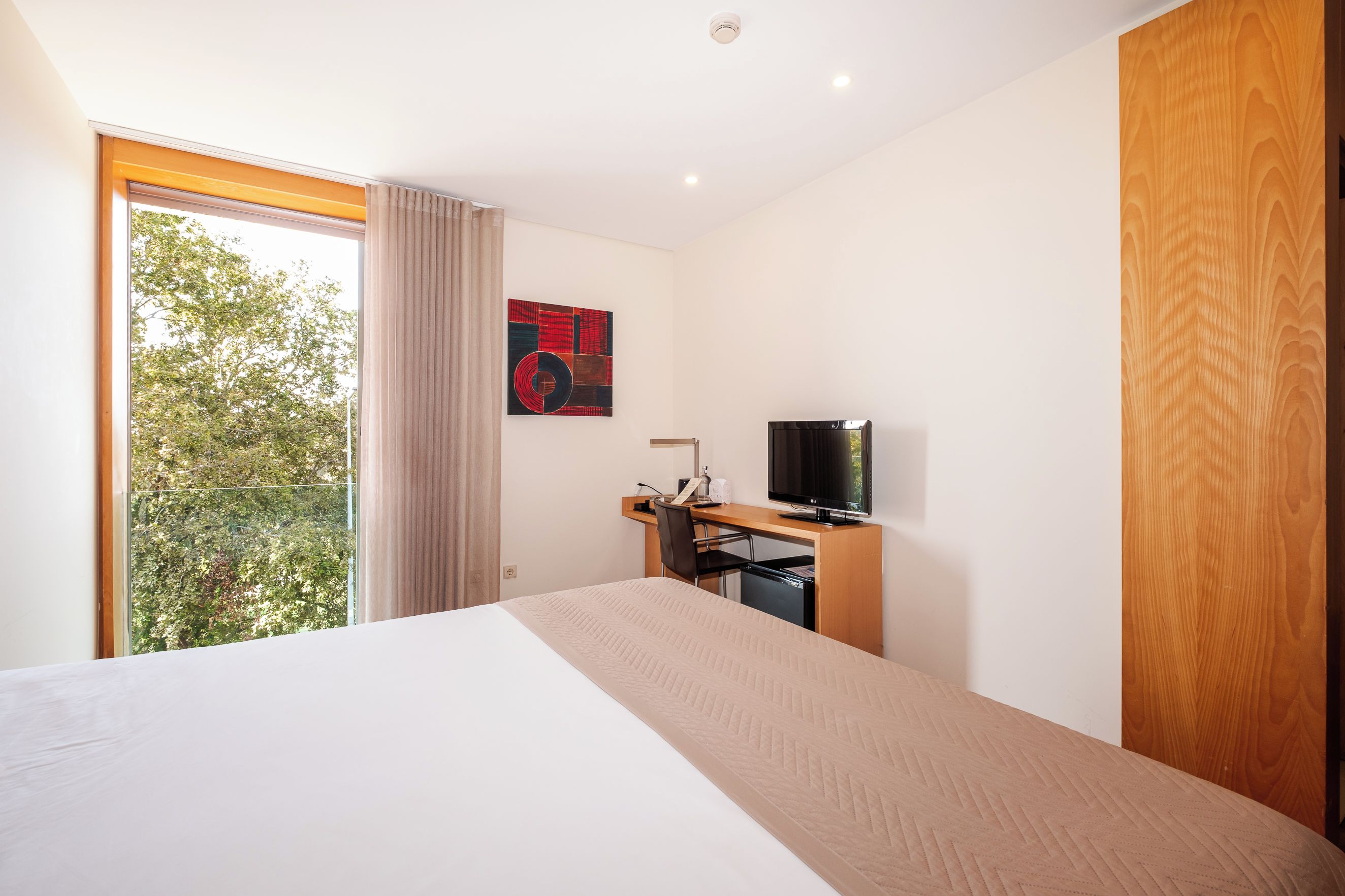 A hotel room with a large bed, a desk with a computer, a television, and a window with curtains.