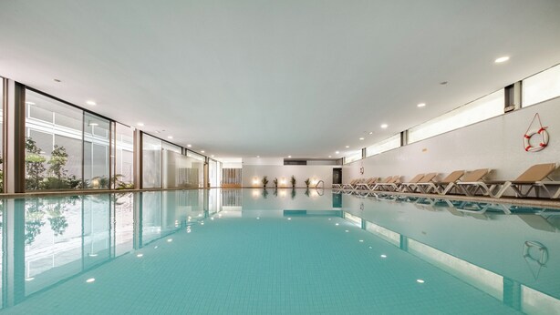 A large indoor swimming pool with clear blue water, sun loungers along the right side, and a lifebuoy on the wall. - Axis Ponte de Lima Golf Resort Hotel (Ponte de Lima)