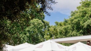 An outdoor seating area with tables and chairs under white umbrellas, set against a stone wall and surrounded by greenery. - Axis Ponte de Lima Golf Resort Hotel (Ponte de Lima)