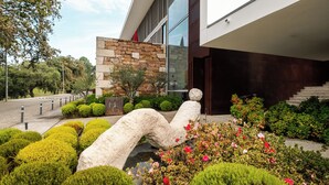 A modern building with a stone facade, a glass entrance, and a landscaped garden with neatly trimmed bushes and flowers. - Axis Ponte de Lima Golf Resort Hotel (Ponte de Lima)